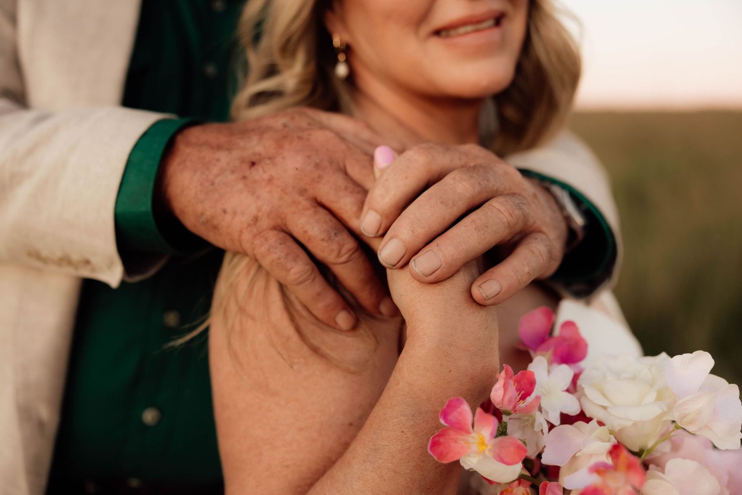 Elderly couple holding hands tenderly, woman holding pink and white flowers, romantic outdoor portrait.