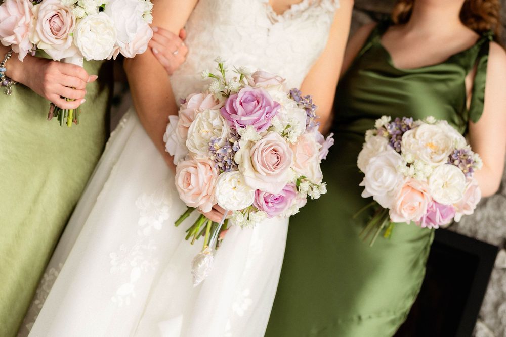 Bride and bridesmaids in green dresses holding pastel pink, white, and lavender rose wedding bouquets.