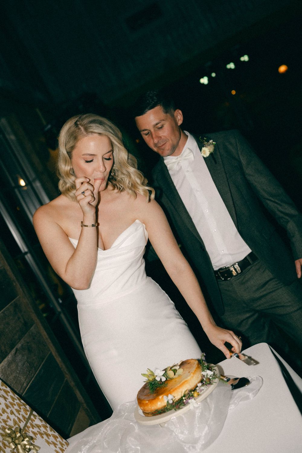Bride and groom cutting wedding cake together at evening reception.
