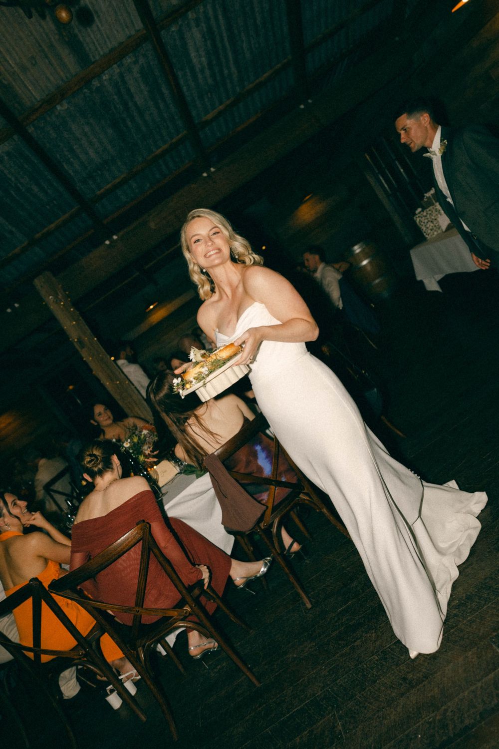 Bride in elegant white gown carrying gift box through wedding reception venue.