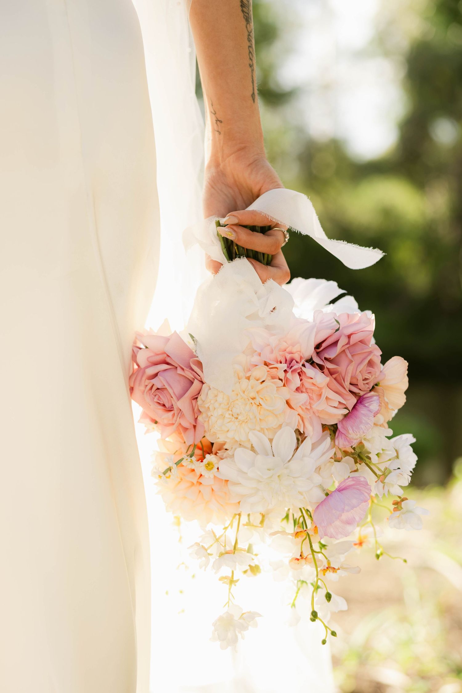 Bride holding a romantic bridal bouquet of pink roses, white chrysanthemums, and blush flowers with ribbon wrap.