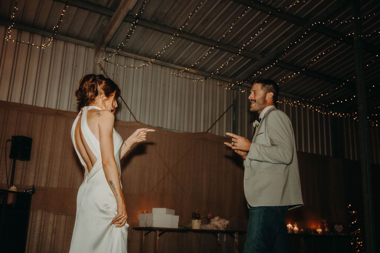 Bride and groom sharing a playful moment on the dance floor in a rustic barn with fairy lights.