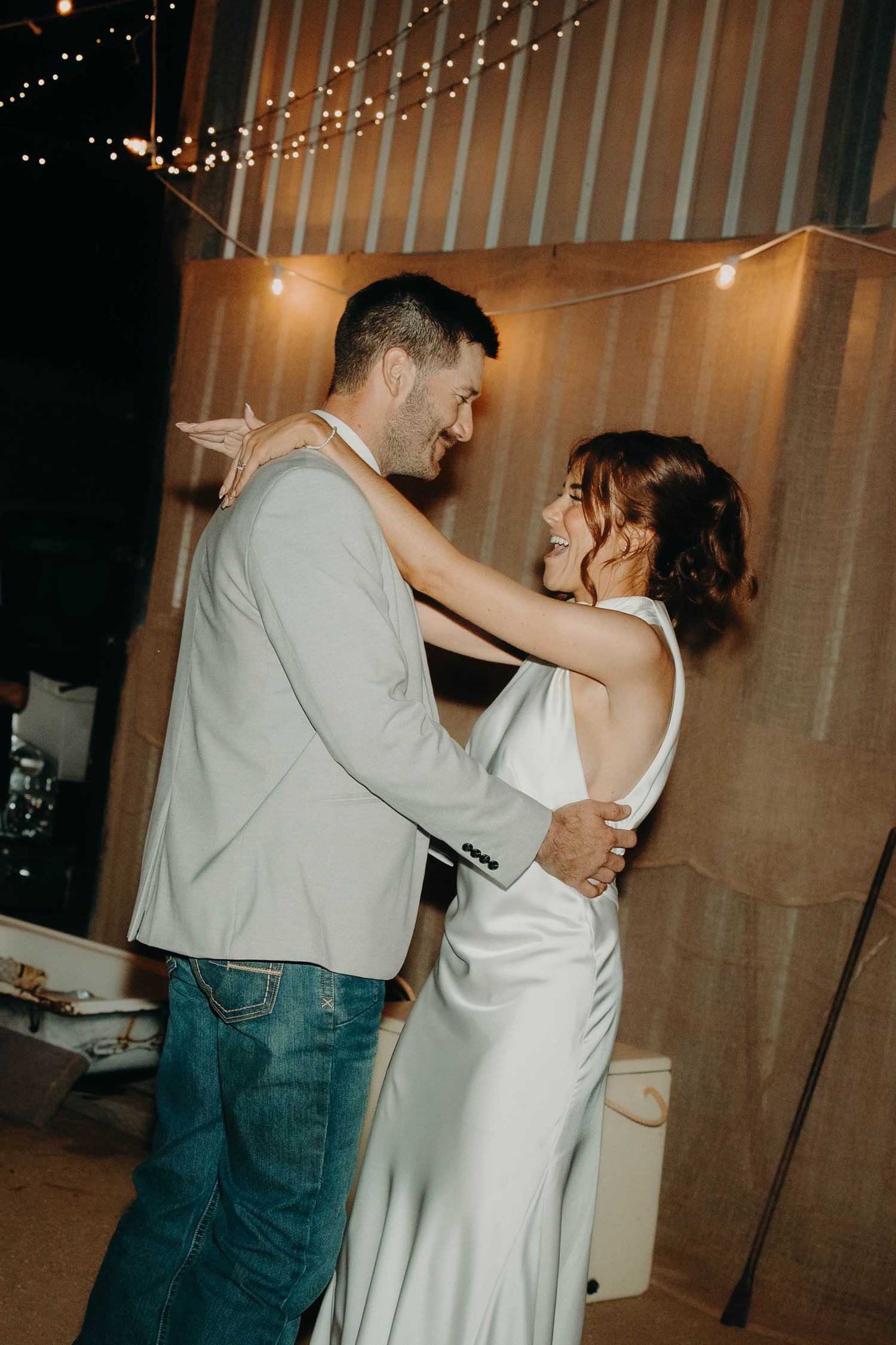 Bride and groom sharing their first dance in a warmly lit rustic barn venue with string lights.