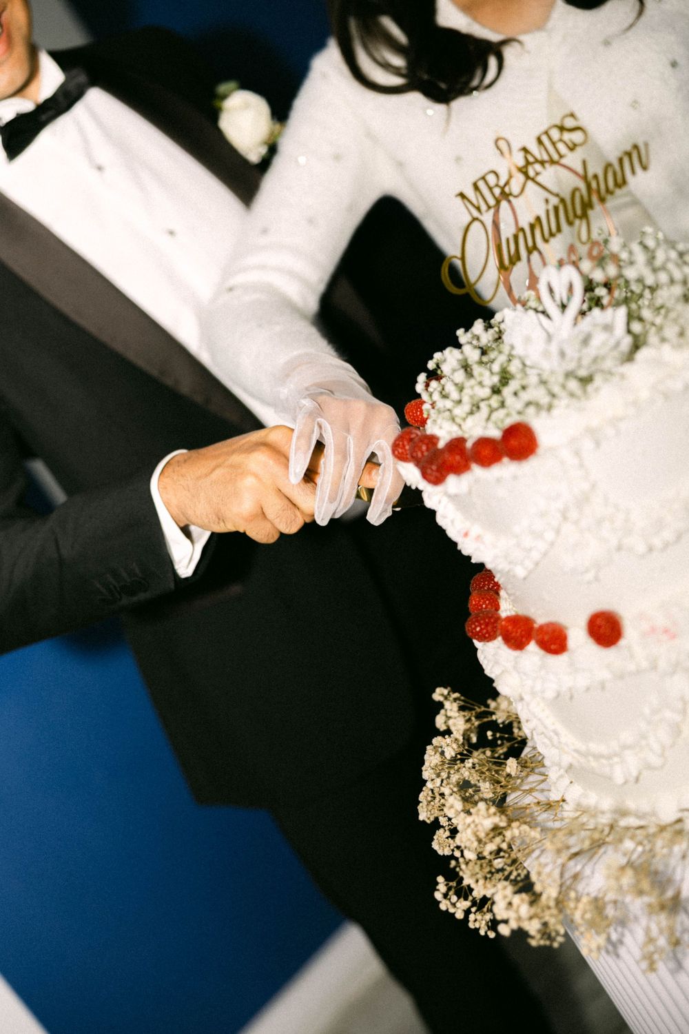 Mr. & Mrs. Cunningham cutting their white wedding cake decorated with raspberries and baby's breath flowers.