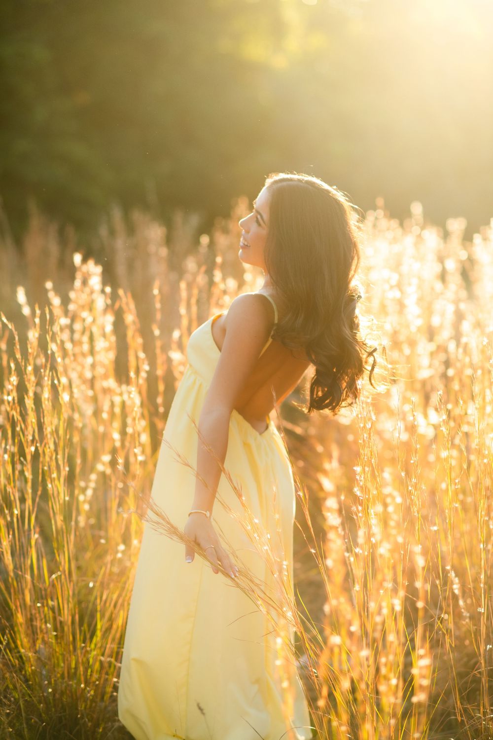 Young woman in yellow sundress basking in warm golden sunset light in field.