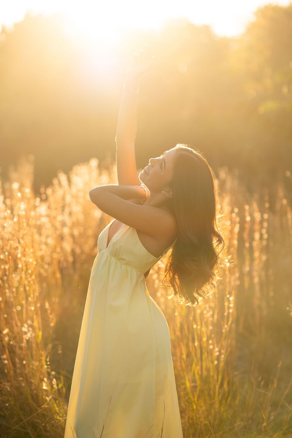 Woman in yellow dress reaching upward with eyes closed in radiant golden sunset field.