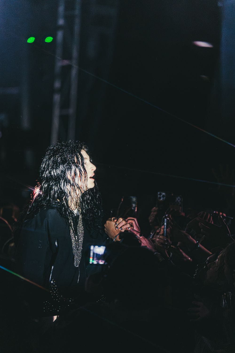 Female performer on dark stage holds fan's hand during live concert with crowd and stage lights.