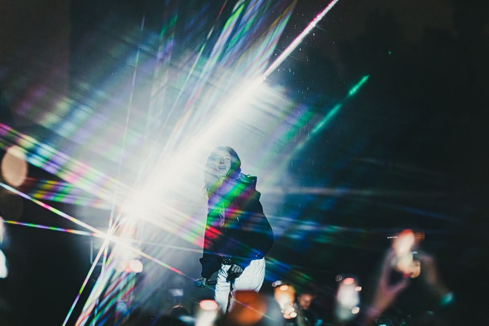 Performer on stage surrounded by colorful laser light beams at a concert event.