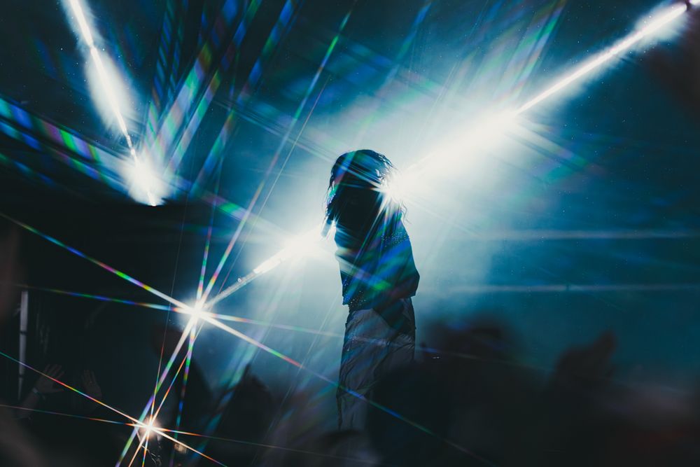 Silhouetted performer on stage surrounded by vibrant blue and white light beams at a live concert.