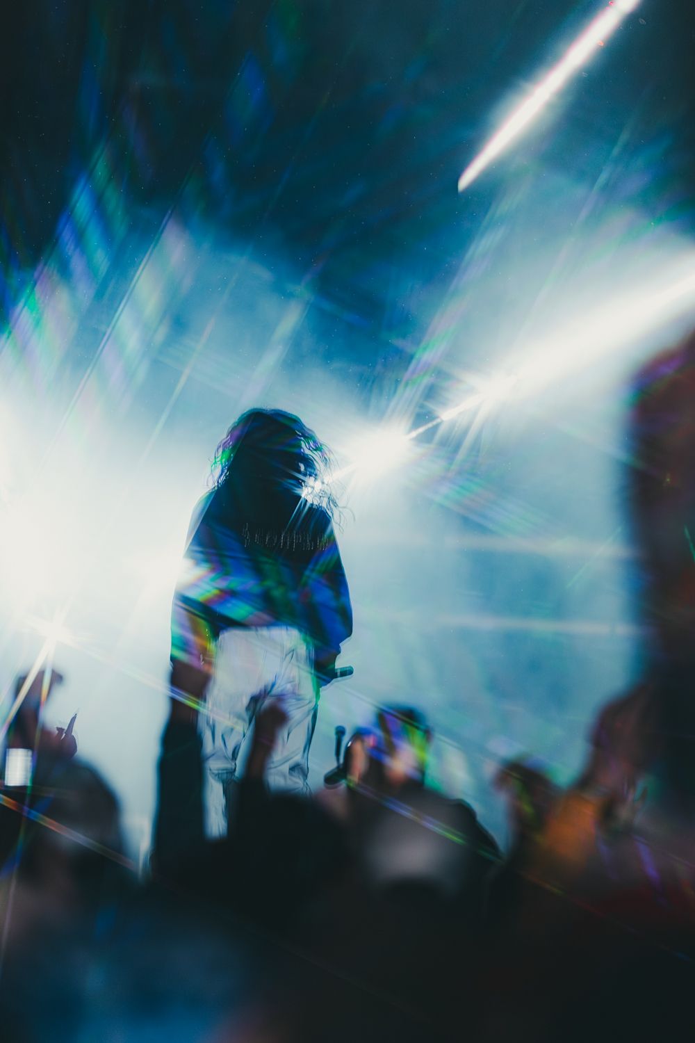 Performer silhouetted on stage with vibrant concert lights and crowd reaching up during a live music event.