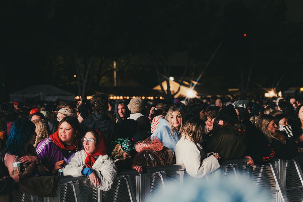 Large crowd of concert-goers gathered behind metal barriers at an outdoor nighttime music festival event.