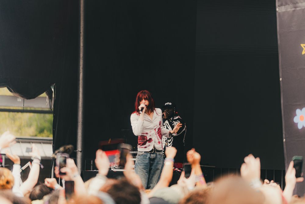 Female singer performing on stage at outdoor music festival with crowd cheering in foreground.