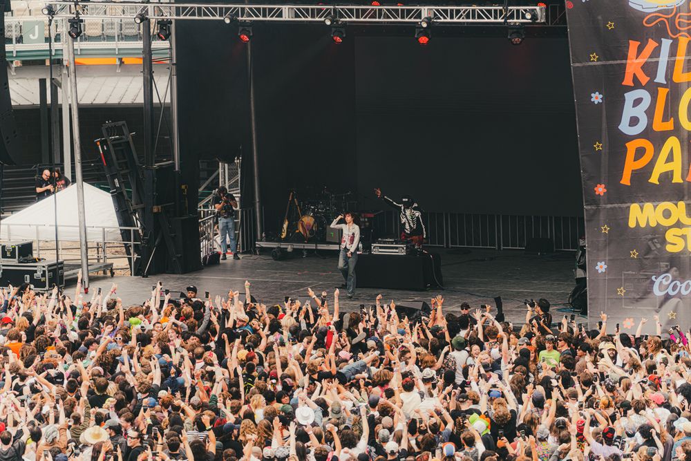 Large crowd at Kid Blue Party music festival with performers on a large outdoor stage with bright lights.