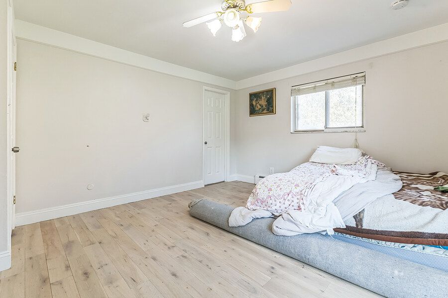 Bright bedroom with light hardwood floors, white walls, ceiling fan, and a mattress on the floor near a window.