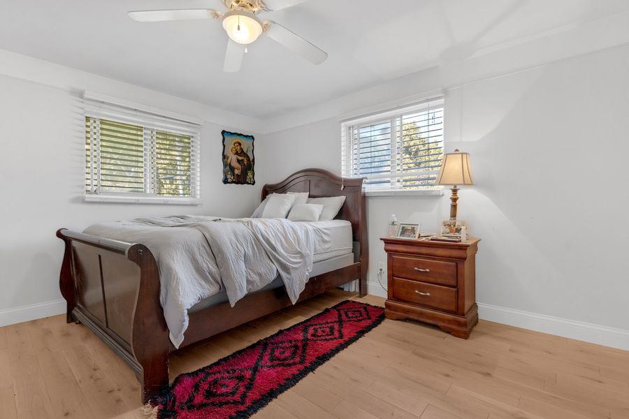 Bright bedroom with sleigh bed, hardwood floors, red rug, ceiling fan, and natural light from two windows.