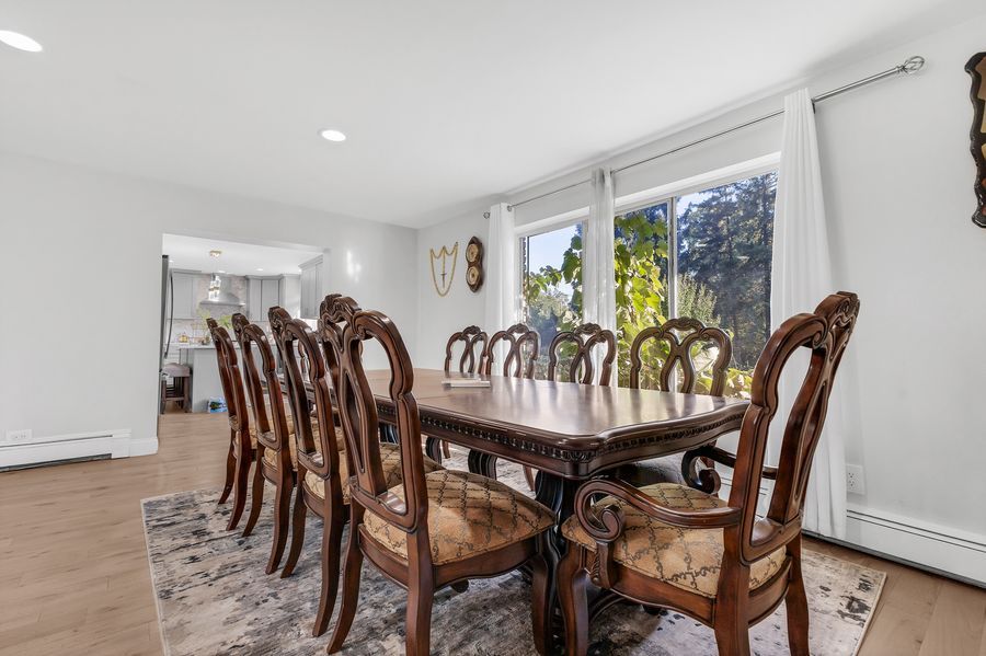 Elegant dining room with ornate dark wood table and chairs, hardwood floors, and large windows with natural light.
