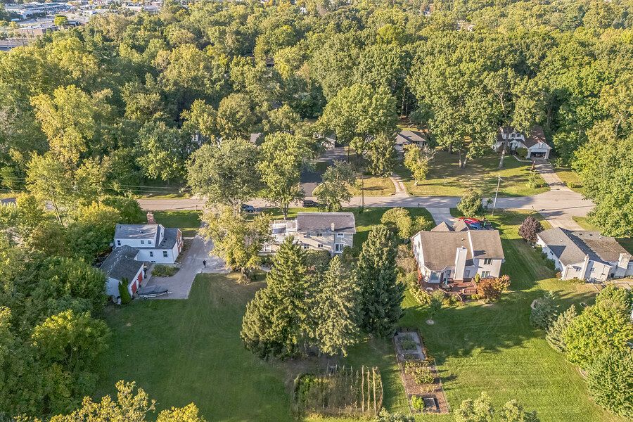 Aerial view of suburban homes surrounded by lush green trees and manicured lawns in a peaceful residential neighborhood.