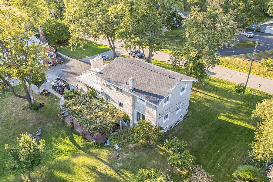 Aerial view of a two-story suburban home surrounded by mature trees and lush green lawn.