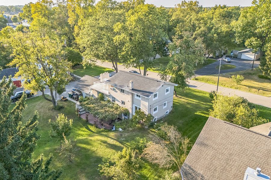 Aerial view of a two-story home surrounded by mature trees with a lush green lawn and nearby street.