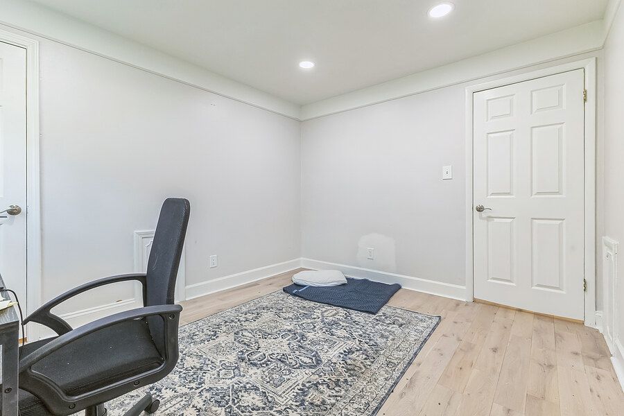 Minimalist home office with black chair, decorative rug, hardwood floors, and white walls with crown molding.