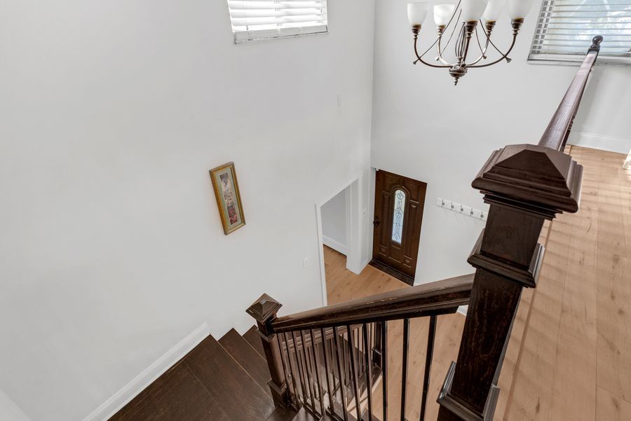 Elegant two-story foyer with dark wood staircase, hardwood floors, chandelier, and white walls leading to a front door.
