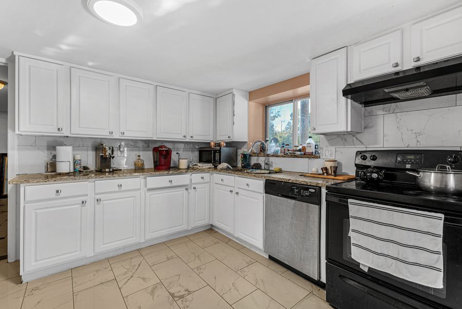 White kitchen with black appliances, tile backsplash, and ample cabinet storage.