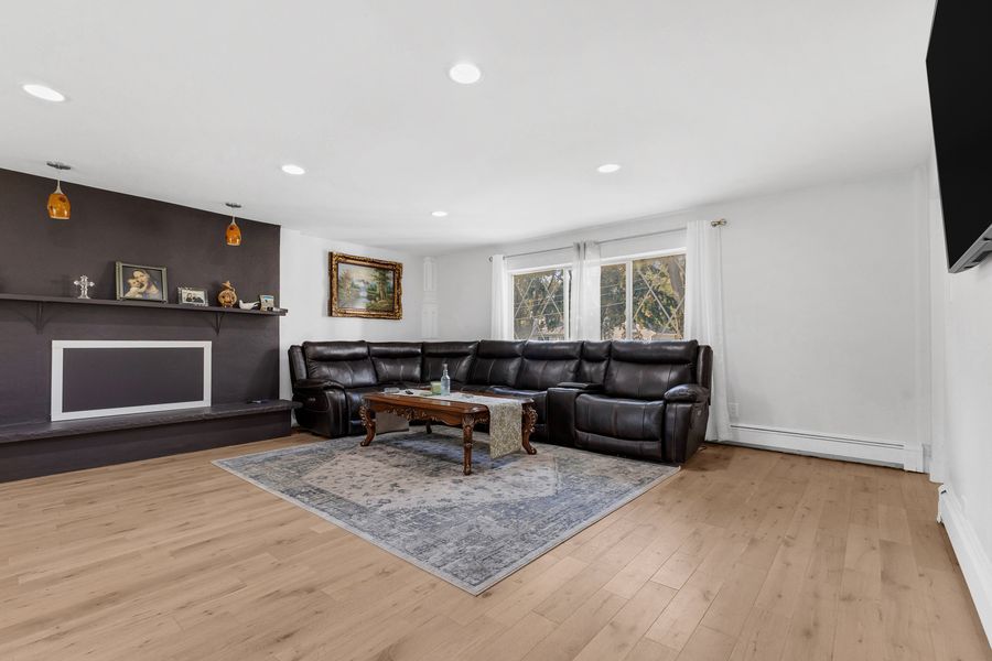 Spacious living room with black leather sectional sofa, hardwood floors, and dark accent wall with built-in shelving.