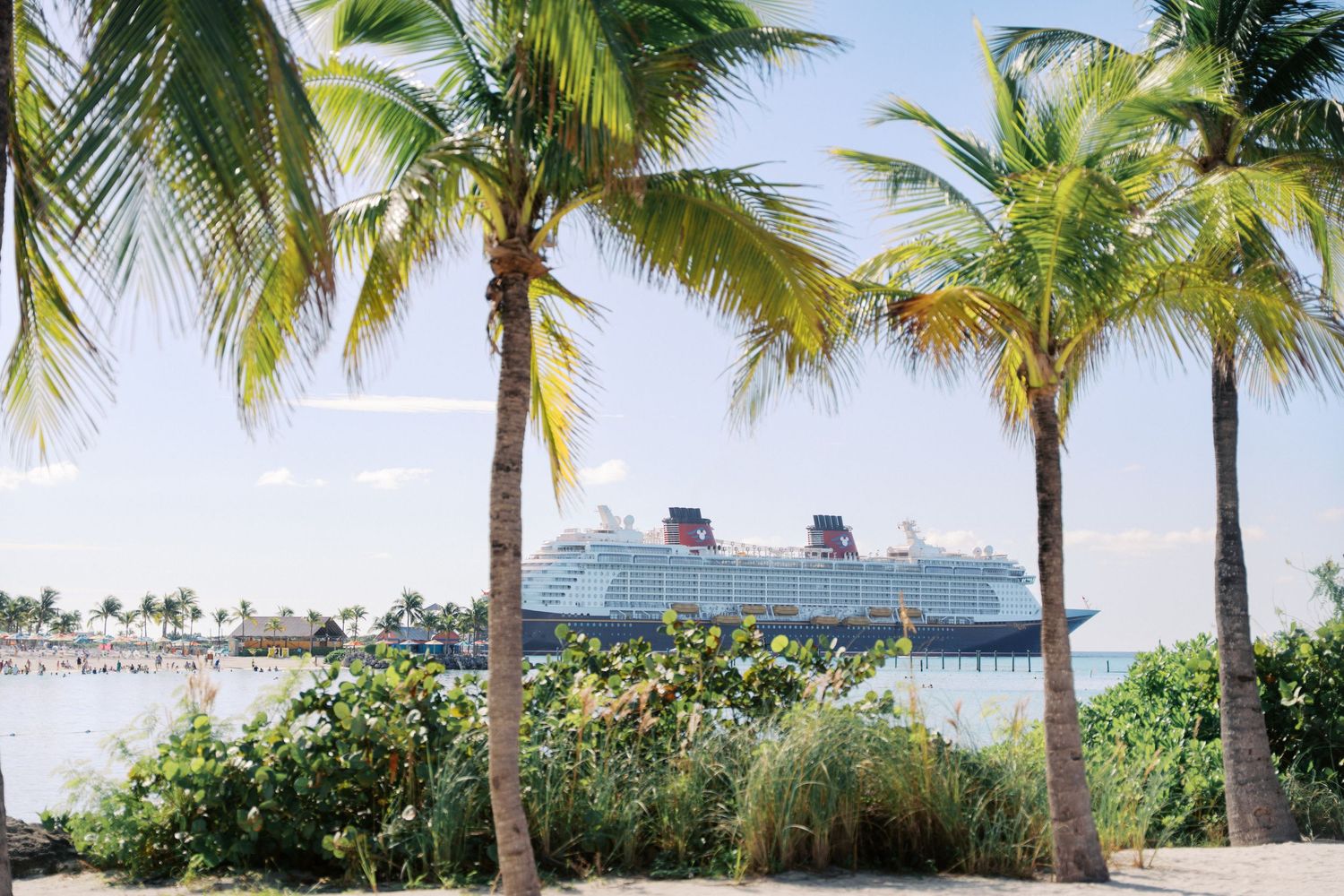 A large Disney cruise ship docked at a tropical island with white sandy beach and clear turquoise water.