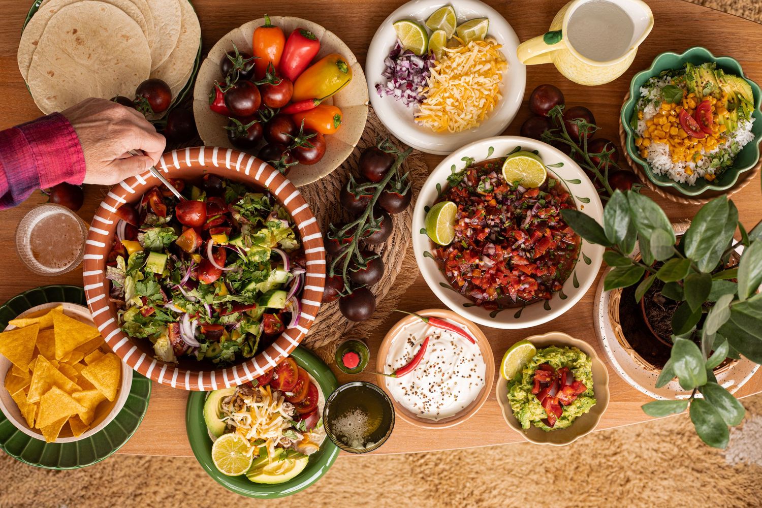 Overhead view of a colorful Mexican food spread with salads, guacamole, chips, and fresh toppings on a wooden table.