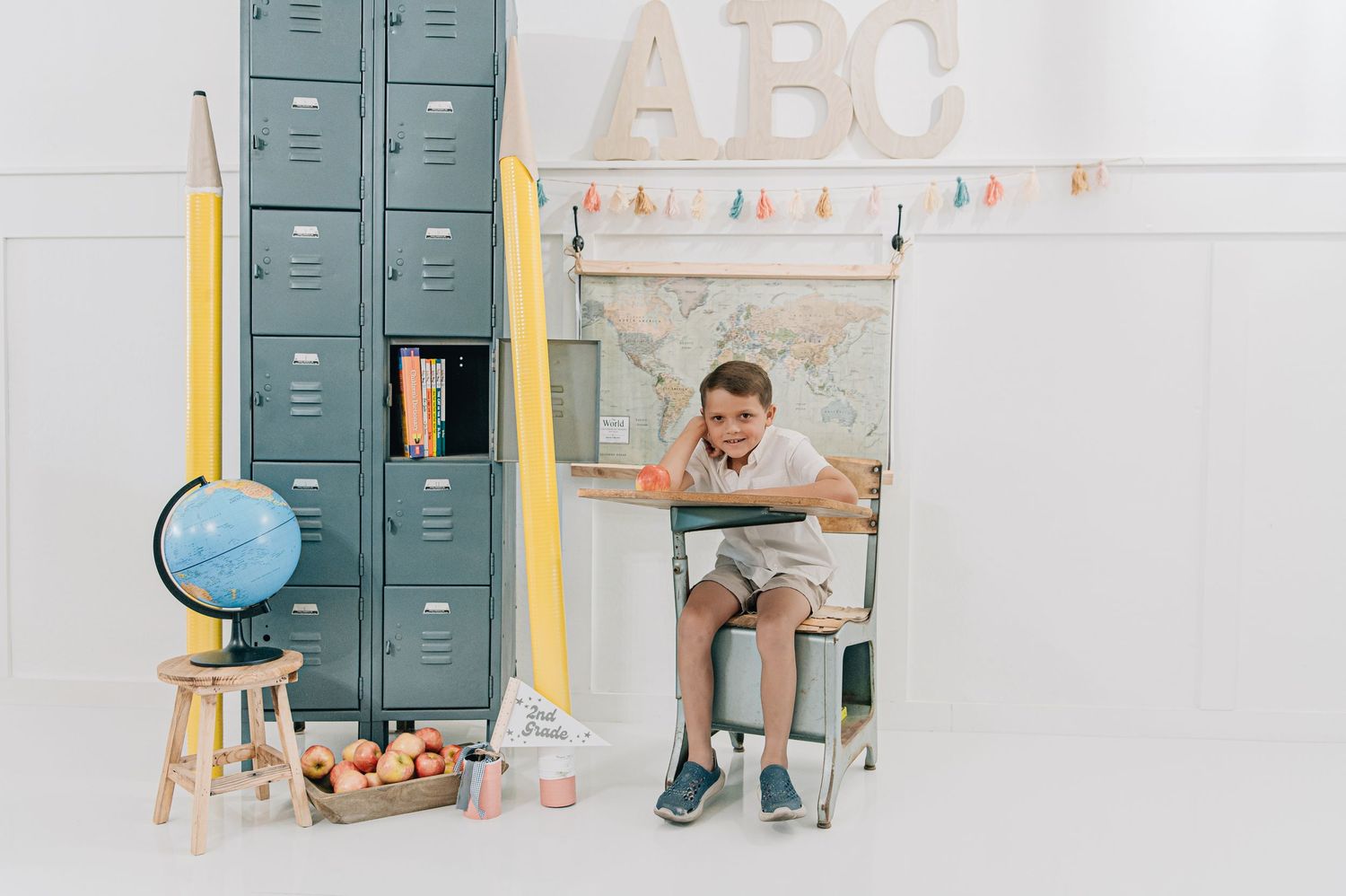 Boy sitting at school desk with globe, apples, and lockers in a back-to-school themed photo with ABC decor. Back to school Arizona