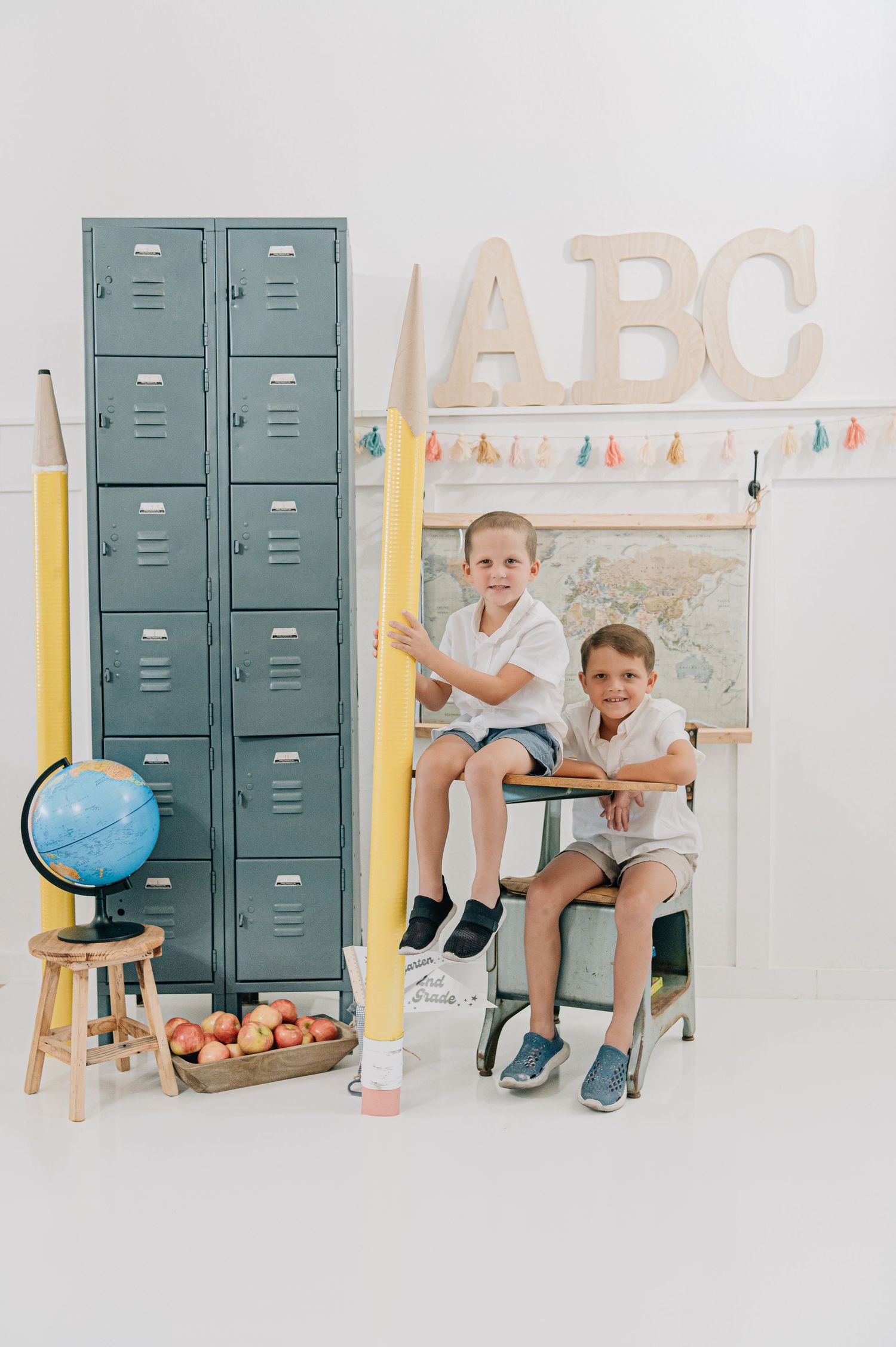 Two boys pose in a school-themed photo with lockers, globe, ABC letters, and oversized pencils. Glendale Peoria Arizona
