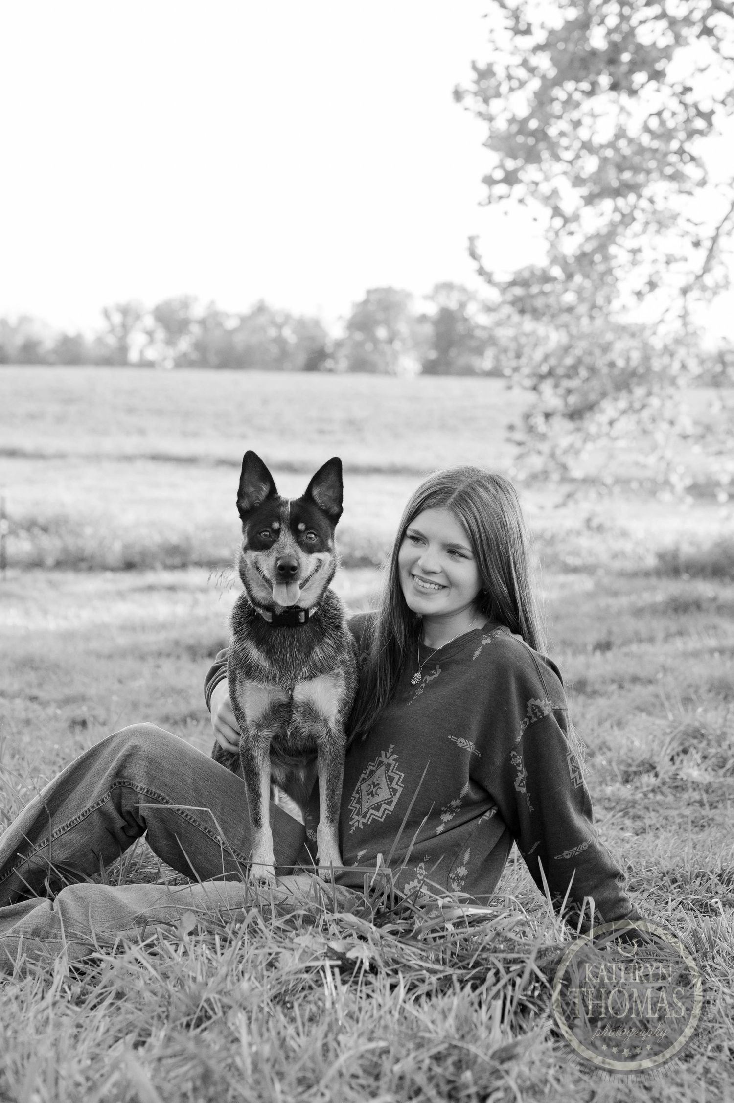 Black and white portrait of a German Shepherd and someone sitting together in a field.