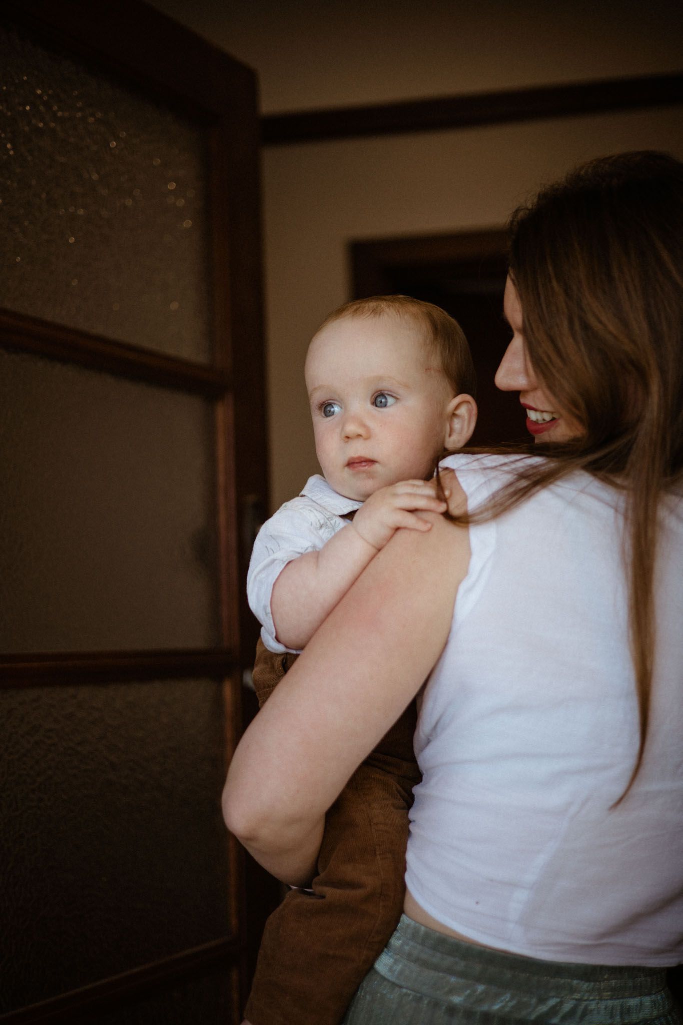 A baby in a light blue outfit being held against a white shirt in a dimly lit indoor setting.