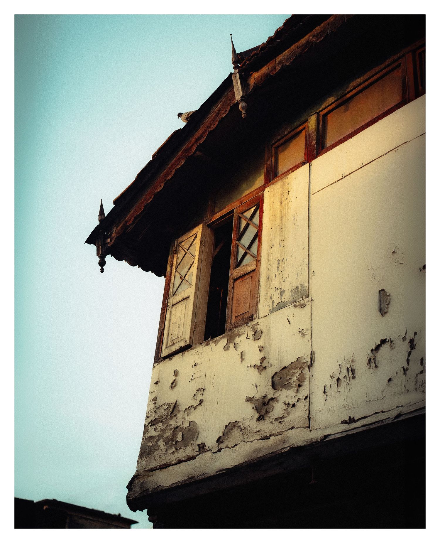 Weathered white building exterior with wooden shutters and peeling paint against a pale sky.
