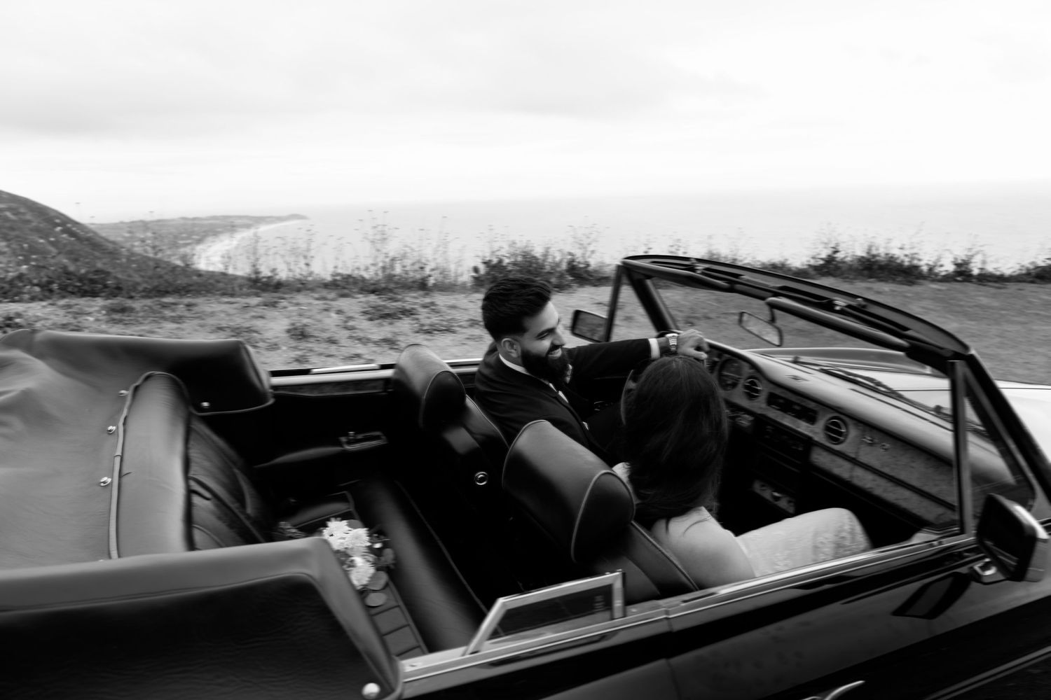 Black and white photo showing interior of a classic convertible car with leather seats against a desert landscape.