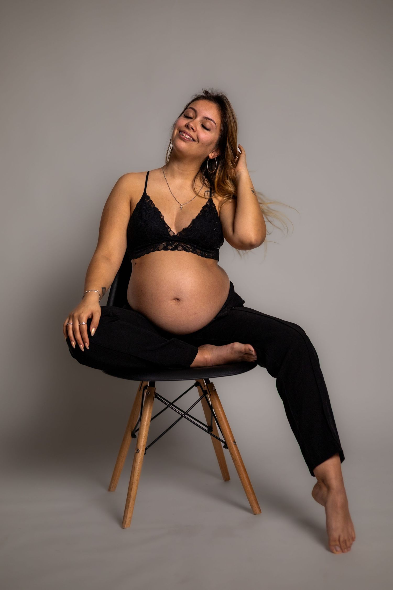 Maternity photo shoot with woman in black outfit posing on wooden chair.