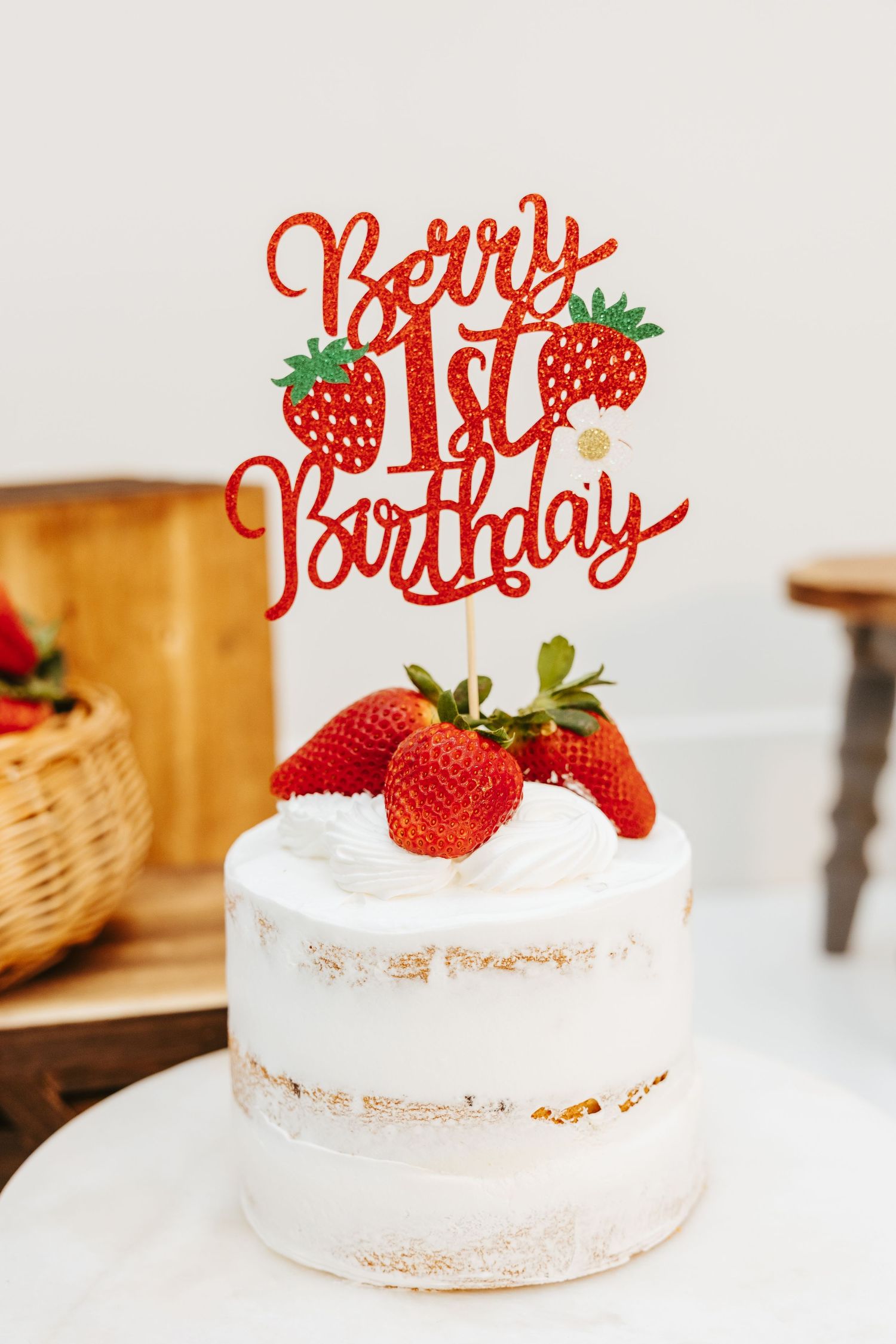 White naked cake topped with fresh strawberries and red 'Berry 1st Birthday' cake topper.