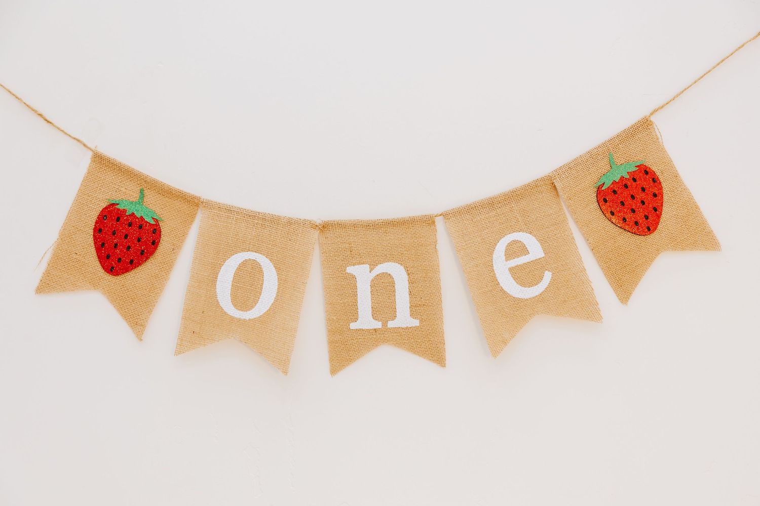 Burlap banner spelling 'one' with red strawberry decorations on each end.