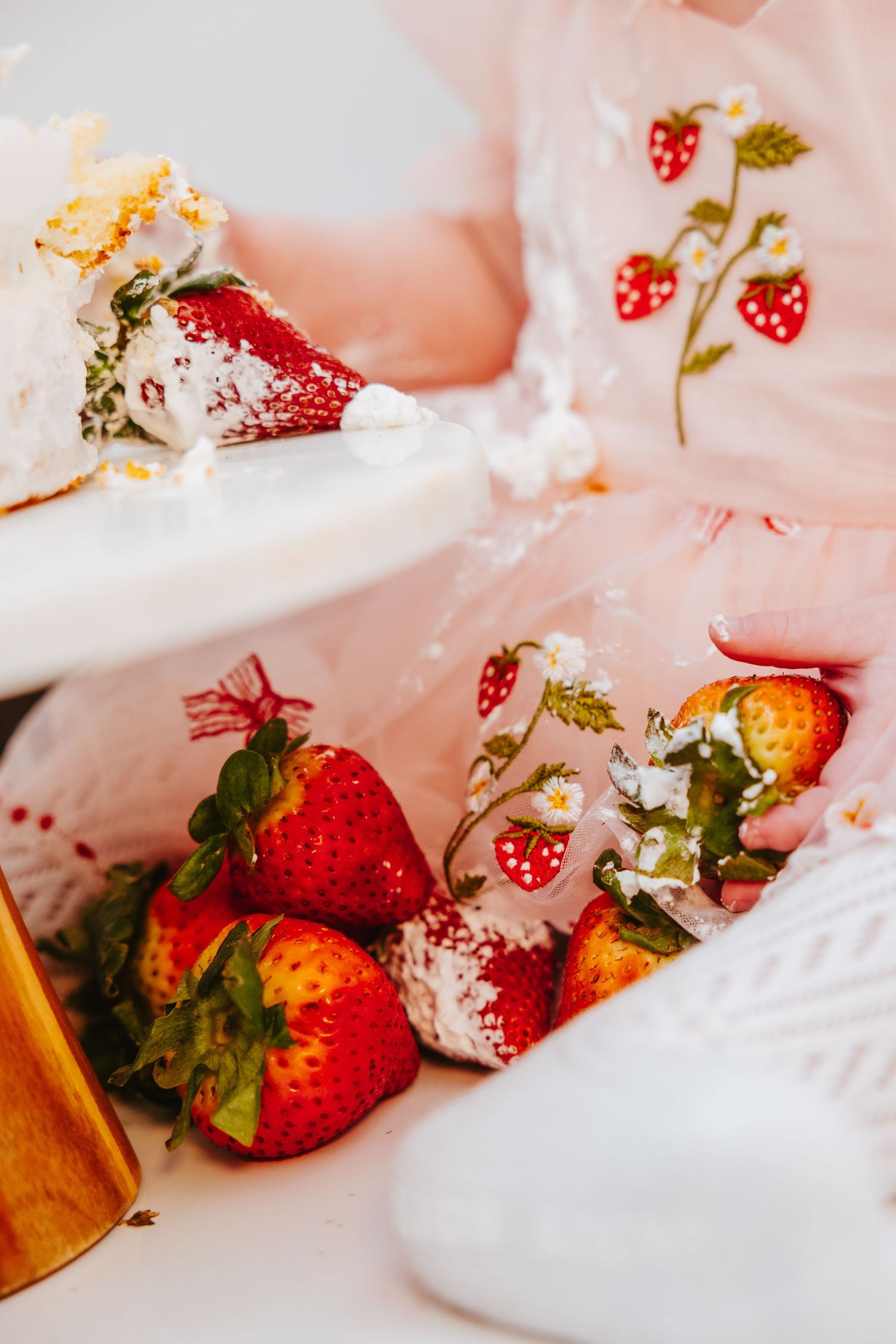 Fresh strawberries and cake crumbs on a white plate with floral dress details.