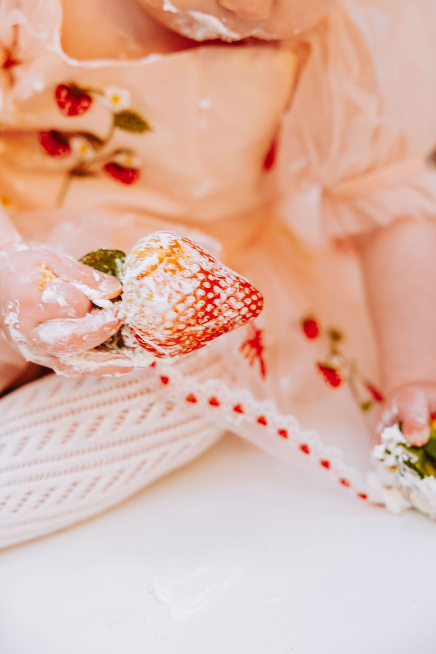 Close-up of a strawberry with whipped cream against pink fabric with floral patterns.