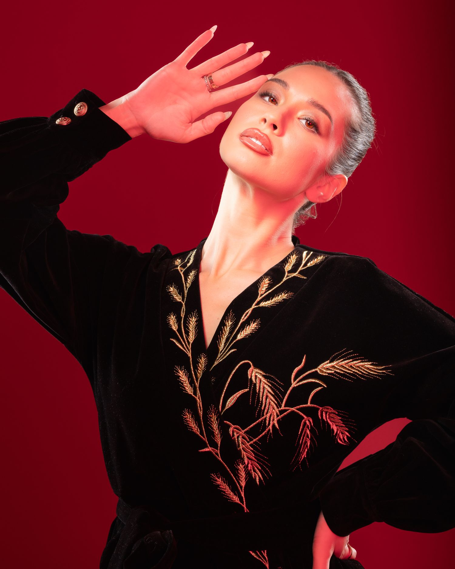 Studio portrait with dramatic orange and purple lighting against a dark background showing an elegant pose and wrist tattoo.