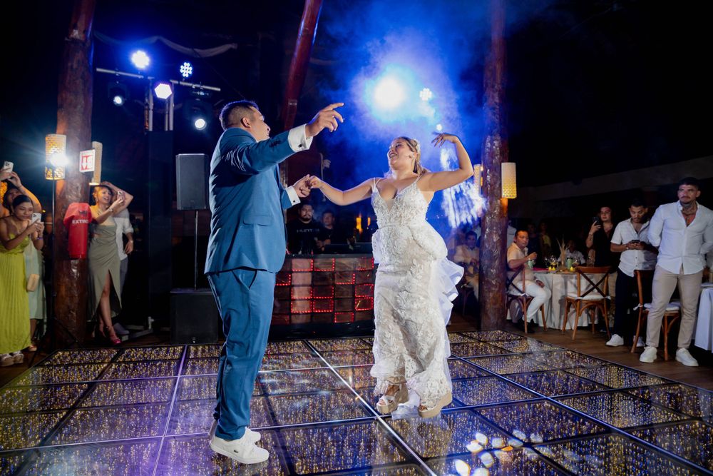 Dancing couple celebrates during their wedding reception on an illuminated dance floor with blue lighting.