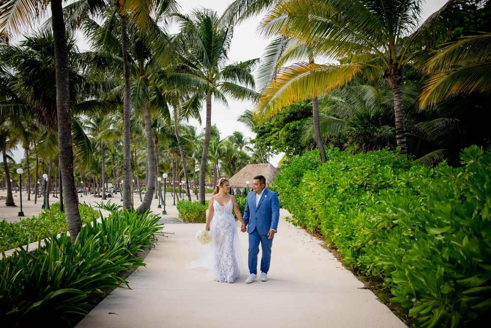 A couple strolls along a palm-lined pathway at a tropical resort wearing formal attire.