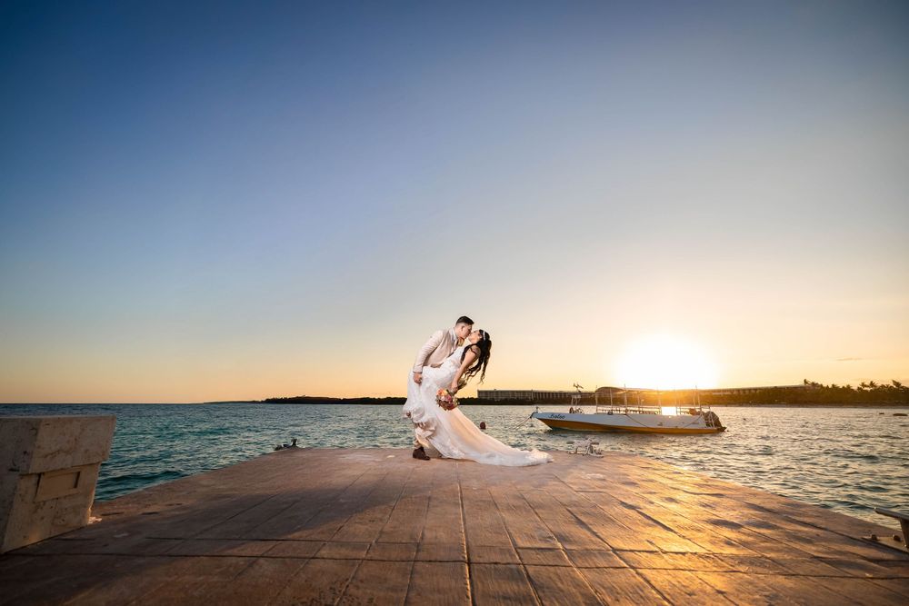 A couple shares a romantic sunset moment on a wooden pier overlooking a tranquil ocean bay.