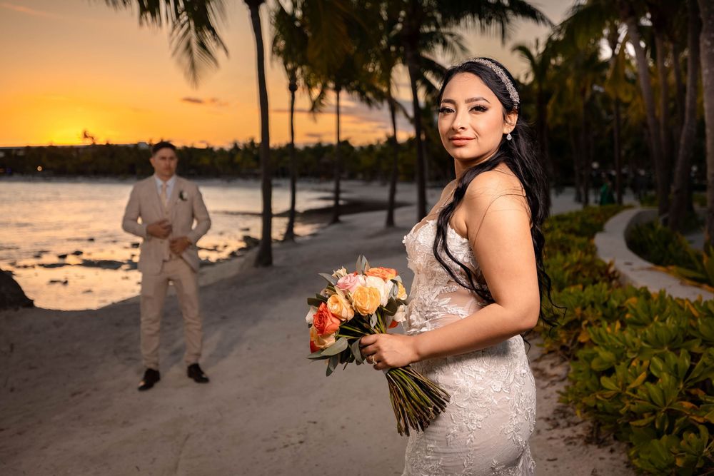 A wedding photoshoot at sunset along a tropical beach with palm trees and orange sky in Hawaii.
