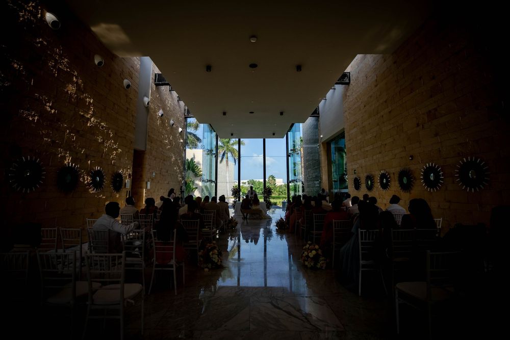 Interior view of a modern wedding ceremony venue with palm trees visible through glass doors at the end of the aisle.