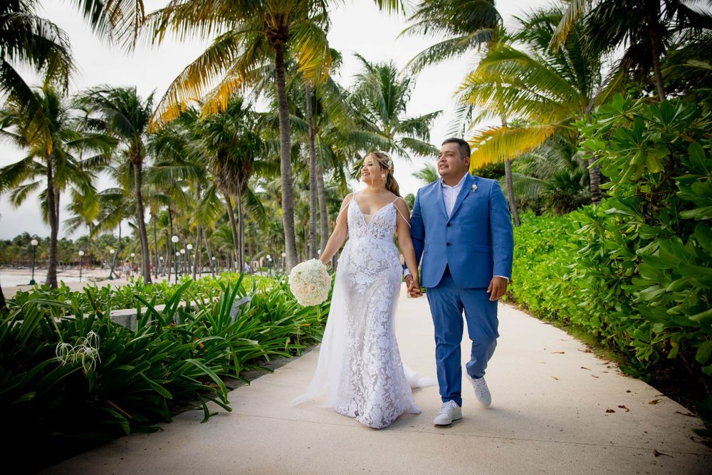 A couple walks hand in hand along a tropical path lined with palm trees and greenery.