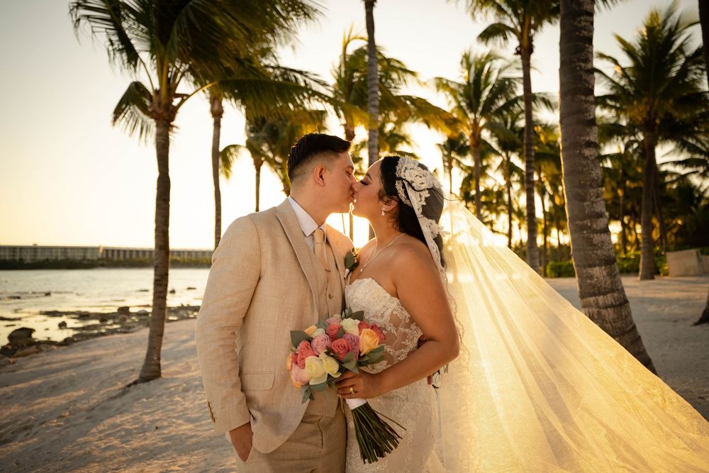 Couple embraces in sunset light on tropical beach with palm trees and soft golden glow.