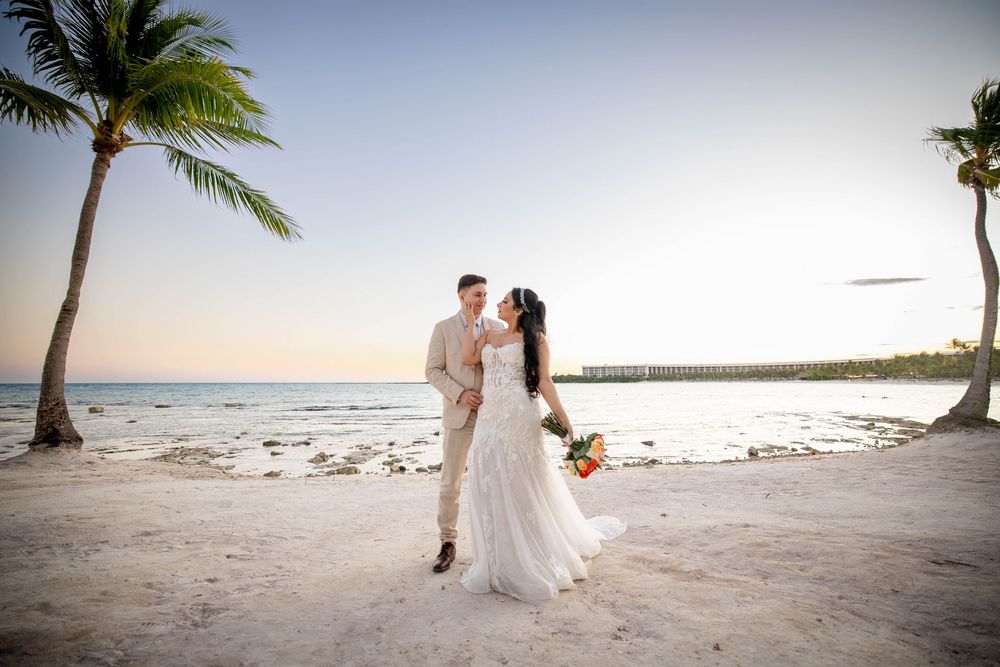 A scenic destination beach wedding ceremony taking place under swaying palm trees at sunset.