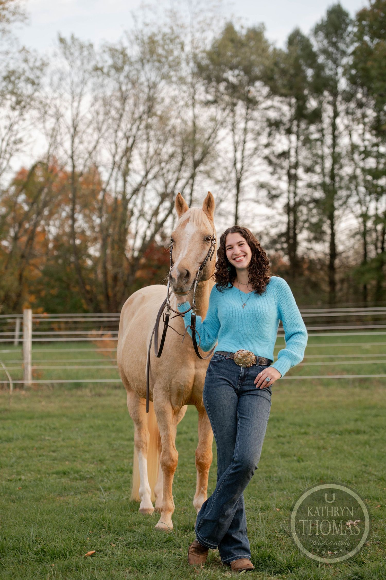 Person and palomino horse pose together in fenced pasture with autumn trees.